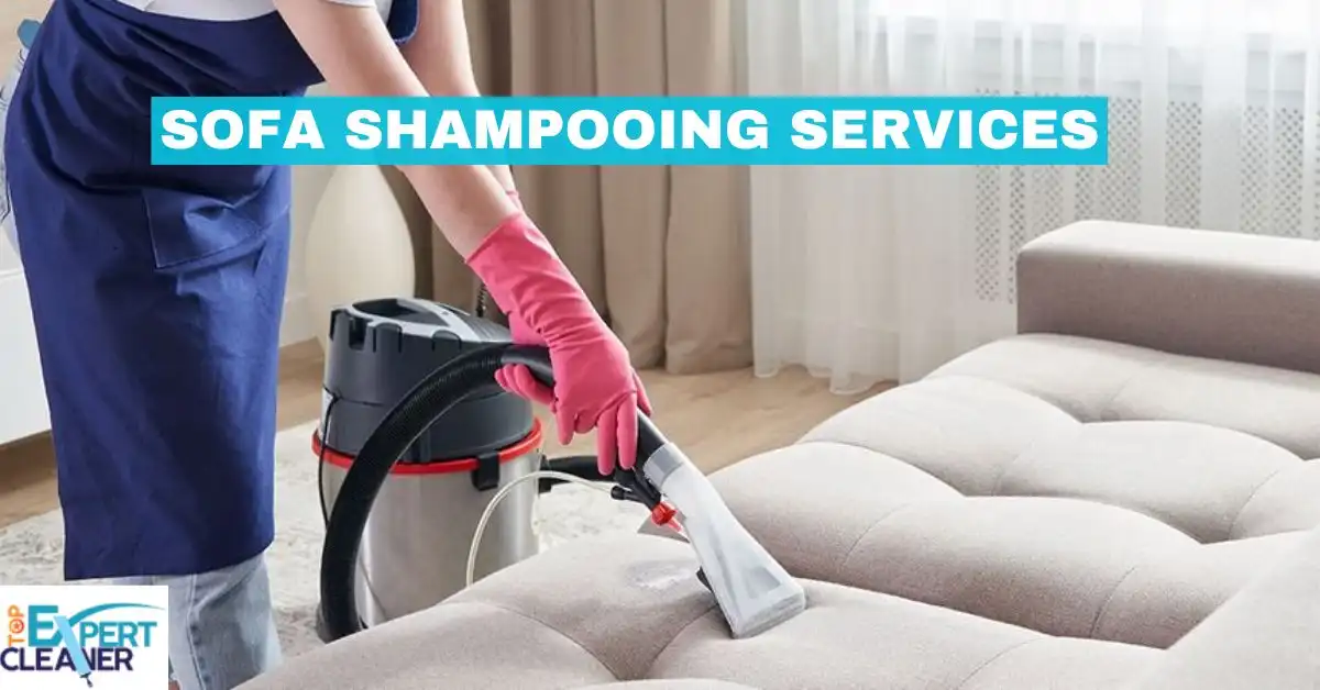 A professional cleaning technician wearing a blue apron and pink gloves is using a wet/dry vacuum cleaner with an upholstery attachment to shampoo and clean a light-colored fabric sofa. The text "SOFA SHAMPOOING SERVICES" is overlaid on the image, along with a logo for "EXPERT TOP CLEANER" in the bottom left corner.
